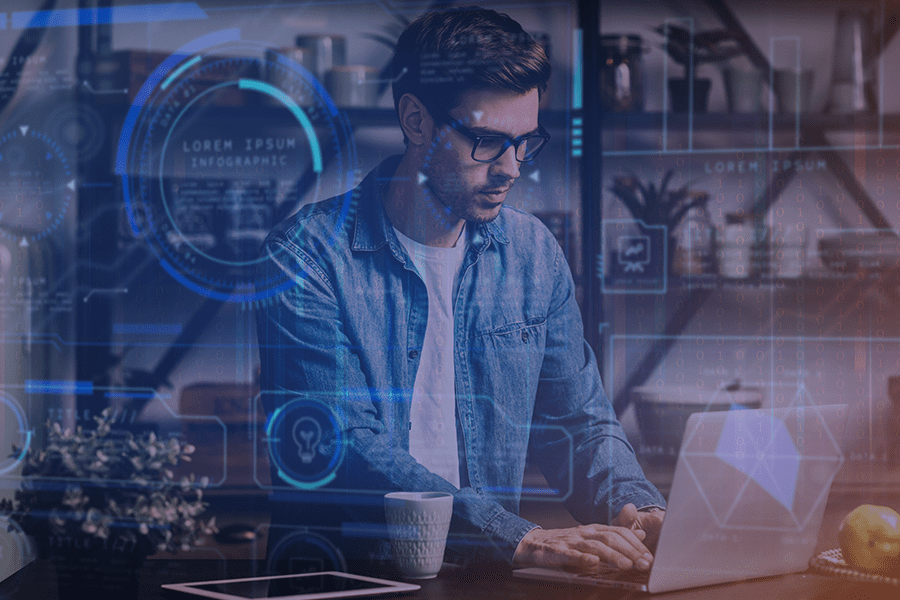 A imagem mostra um homem jovem usando óculos, concentrado enquanto trabalha em um notebook. Ele veste uma camisa jeans azul sobre uma camiseta branca. Sobre a mesa, há uma xícara branca e, ao fundo, prateleiras com plantas e objetos decorativos, sugerindo um ambiente moderno e aconchegante. Na frente da cena, foram aplicados efeitos gráficos digitais em azul, com ícones de tecnologia, hologramas, diagramas e códigos binários, dando a impressão de que o homem está imerso em um ambiente virtual ou futurista, trabalhando com dados ou sistemas digitais.