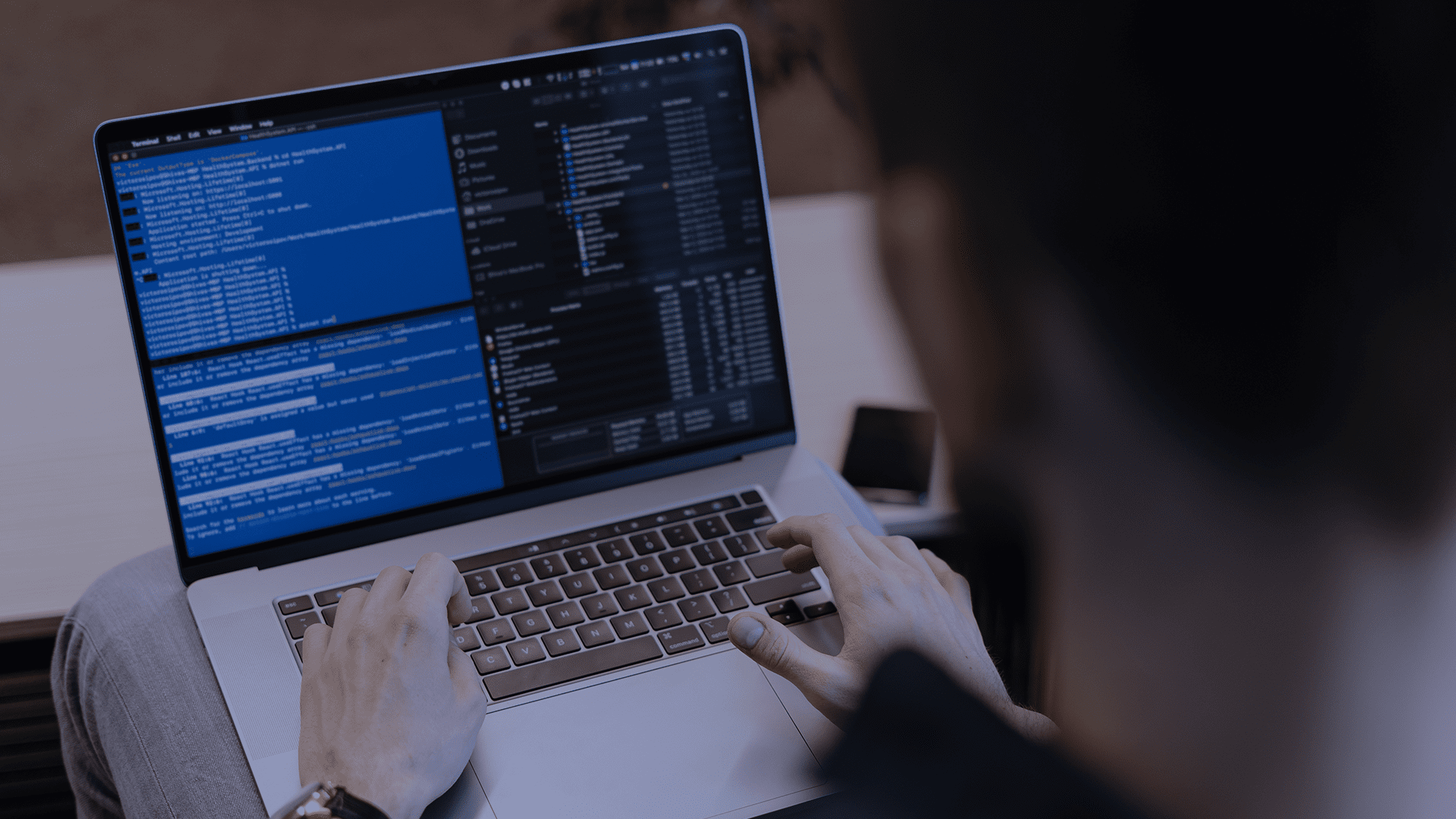 Homem digitando em um notebook com a tela dividida entre códigos e arquivos, em ambiente de trabalho com foco em desenvolvimento de software.