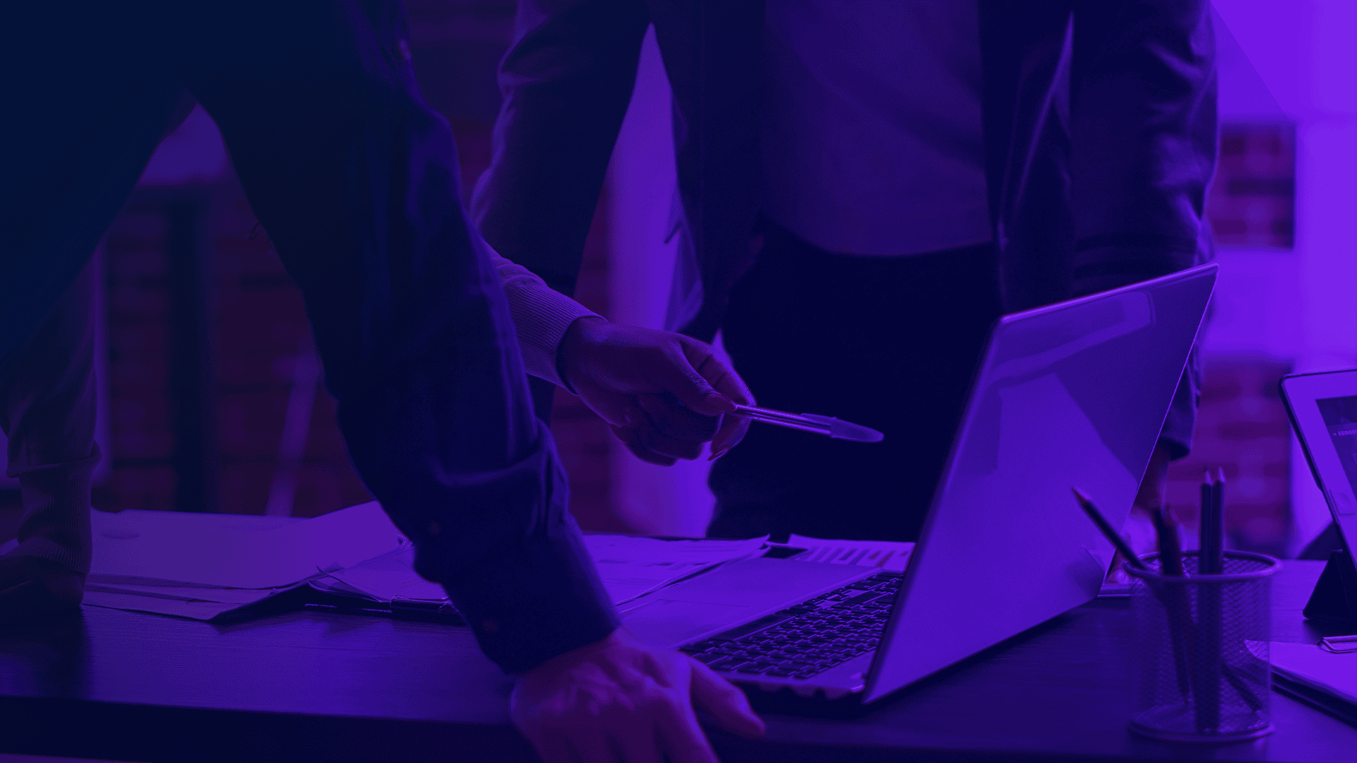 observabilidade full-stack. Pessoas reunidas em torno de um notebook, analisando dados e discutindo soluções em ambiente corporativo com iluminação roxa.